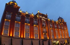 A large, historic building with multiple arched windows and a prominent dome on the right.