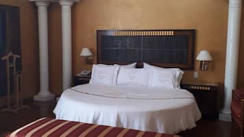 A hotel room with a large bed, two bedside lamps, a wooden bench, and a large framed artwork on the wall.