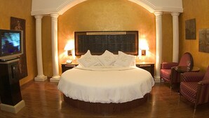 A large bed with a headboard, two bedside lamps, a television on a stand, and two chairs. - Villas Princess Hotel (Mexico City)