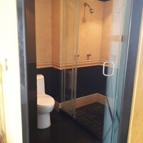 Cabina de ducha con paredes de vidrio, inodoro blanco y suelo oscuro.