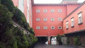 A courtyard with a red building, a gated entrance, and neatly trimmed bushes. - Villas Princess Hotel (Mexico City)