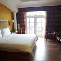 Une chambre d’hôtel avec un grand lit, un bureau et une chaise. Il y a une fenêtre avec des rideaux et une vue sur l’extérieur.