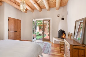A bedroom with a bed, a wooden wardrobe, a fireplace, and a view of the outside garden.