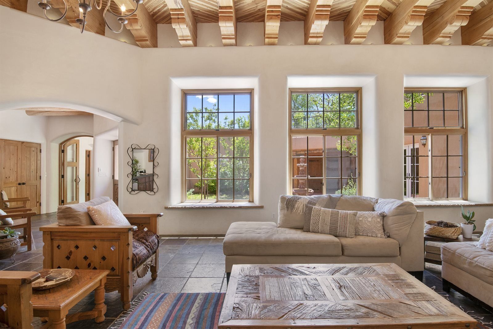A spacious living room with a high ceiling, large windows, a wooden ceiling, and a cozy seating area with a sofa and a coffee table.