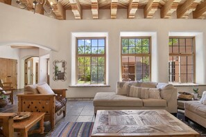 A spacious living room with a high ceiling, large windows, a wooden ceiling, and a cozy seating area with a sofa and a coffee table.