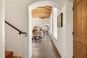 A hallway with a wooden ceiling, stone flooring, and a staircase on the left.