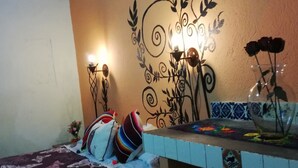 A bedroom with a bed, a nightstand, a decorative wall, and a small table with a vase. - Casa de Huespedes Independencia (San Miguel de Allende)