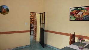 A room with a dining table, chairs, a vase with flowers, a fruit painting, and a door leading to another room. - Casa de Huespedes Independencia (San Miguel de Allende)