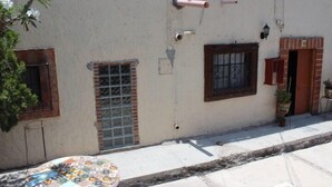 A building with a tiled patio, a window with a metal grill, and a door with a red frame. - Casa de Huespedes Independencia (San Miguel de Allende)