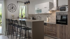 A modern kitchen with a central island, bar stools, a clock, and a view of greenery outside. - Wonderful private villa for 8 guests with WIFI, private pool, A/C, TV, terrace and pets allowed (Rijeka)