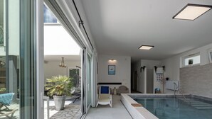 A modern indoor swimming pool with a glass enclosure, a lounge area with a chair and a small table, and a view of the outside patio. - Wonderful private villa for 8 guests with WIFI, private pool, A/C, TV, terrace and pets allowed (Rijeka)