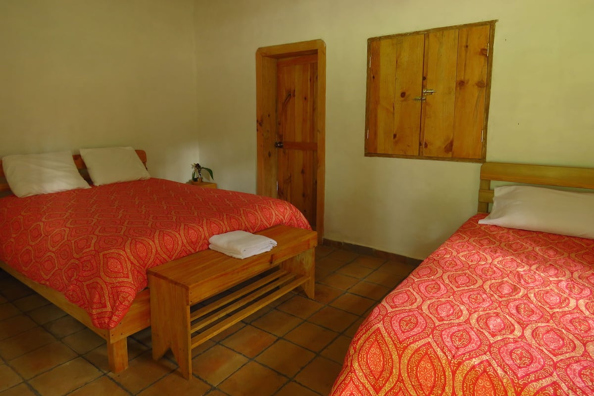 Ein Schlafzimmer mit zwei Betten, Holz-Kopfteilen, einer Bank und einem Holzschrank.