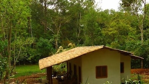 A small, single-story building with a tiled roof, surrounded by a landscaped garden with various plants and a stone pathway. - Ecofinca Luna del Puente (Santa Cruz de Yojoa)