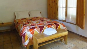 A bedroom with a bed, wooden bench, and two windows with wooden shutters. - Ecofinca Luna del Puente (Santa Cruz de Yojoa)