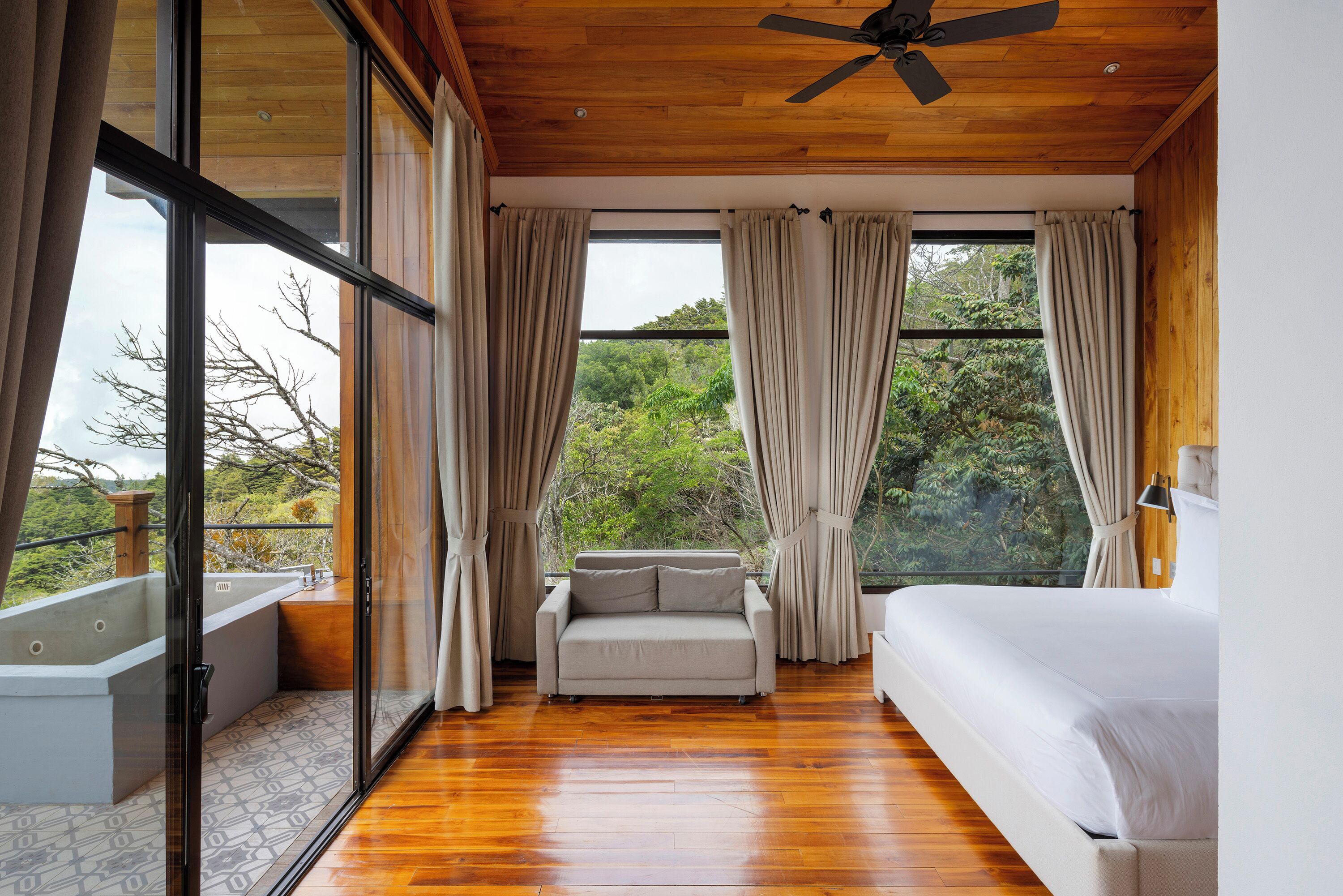 Un dormitorio con una cama grande, un sofá y vistas a la vegetación exterior.