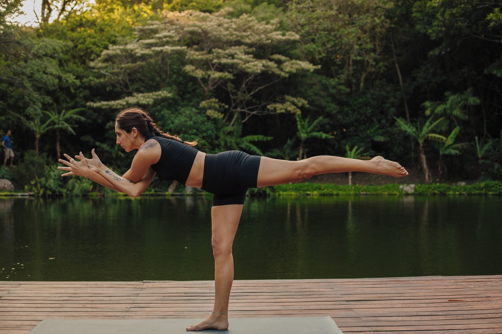 A person performing a yoga pose on a wooden deck by a body of water.