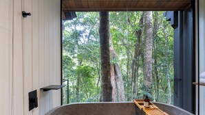 Une salle de bain moderne avec une grande baignoire, un plateau en bois et une vue sur une forêt par une grande fenêtre.
