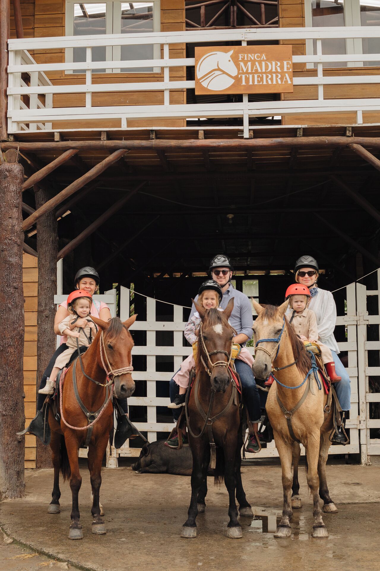 A stable with a sign reading 'FINCA MADRE TERRA' and people riding horses.