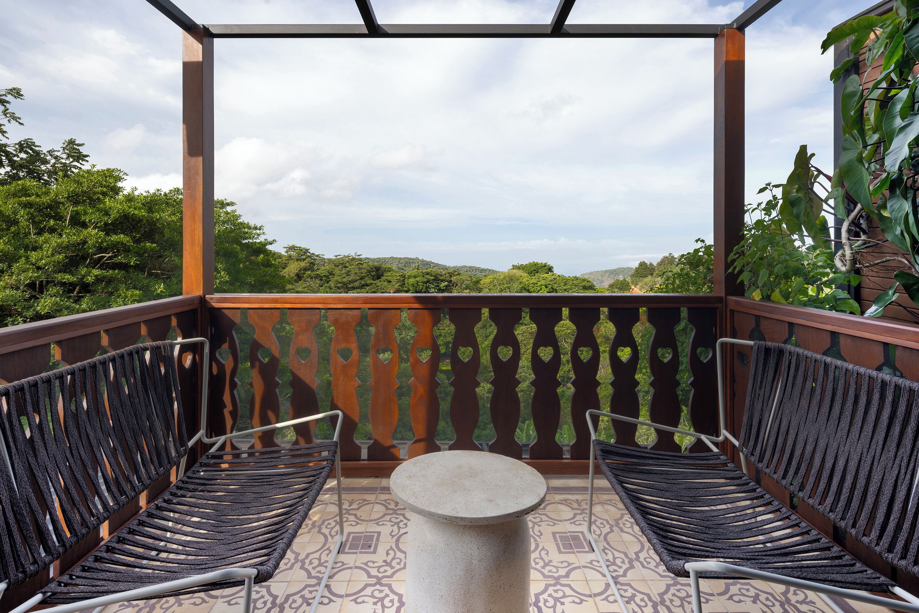 A balcony with two chairs and a table, overlooking a lush green landscape.