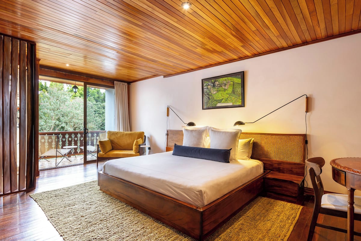 Une chambre spacieuse avec un grand lit, un plafond en bois et un balcon aménagé avec du mobilier d’extérieur.