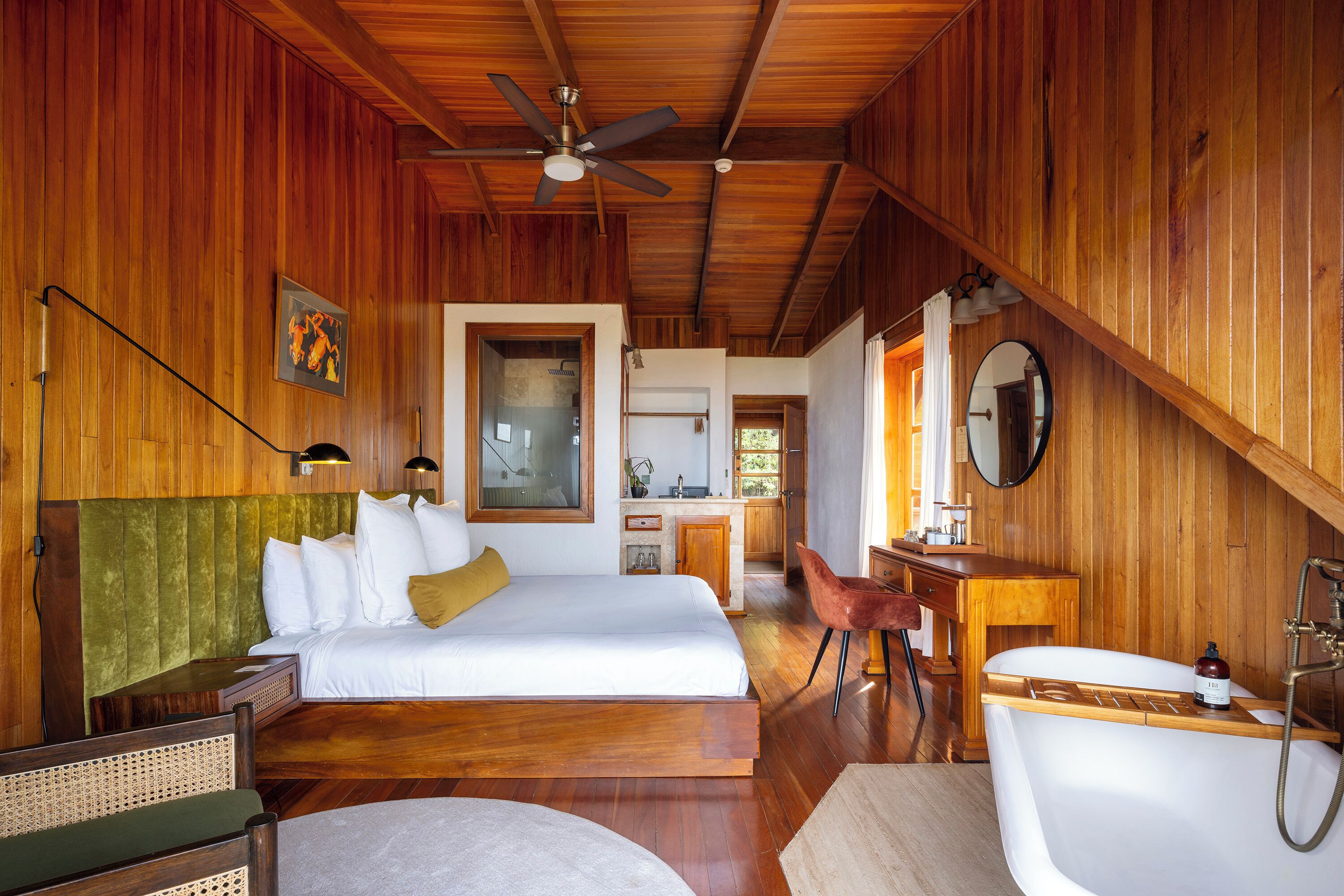 A wooden interior with a bed, desk, and bathtub.