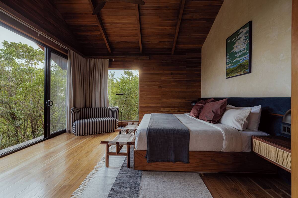 Une chambre avec une grande fenêtre, un lit, un banc et un canapé.