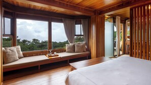 Une chambre dotée d’un grand lit, d’un banc en bois agrémenté de coussins et offrant une vue sur l’extérieur.