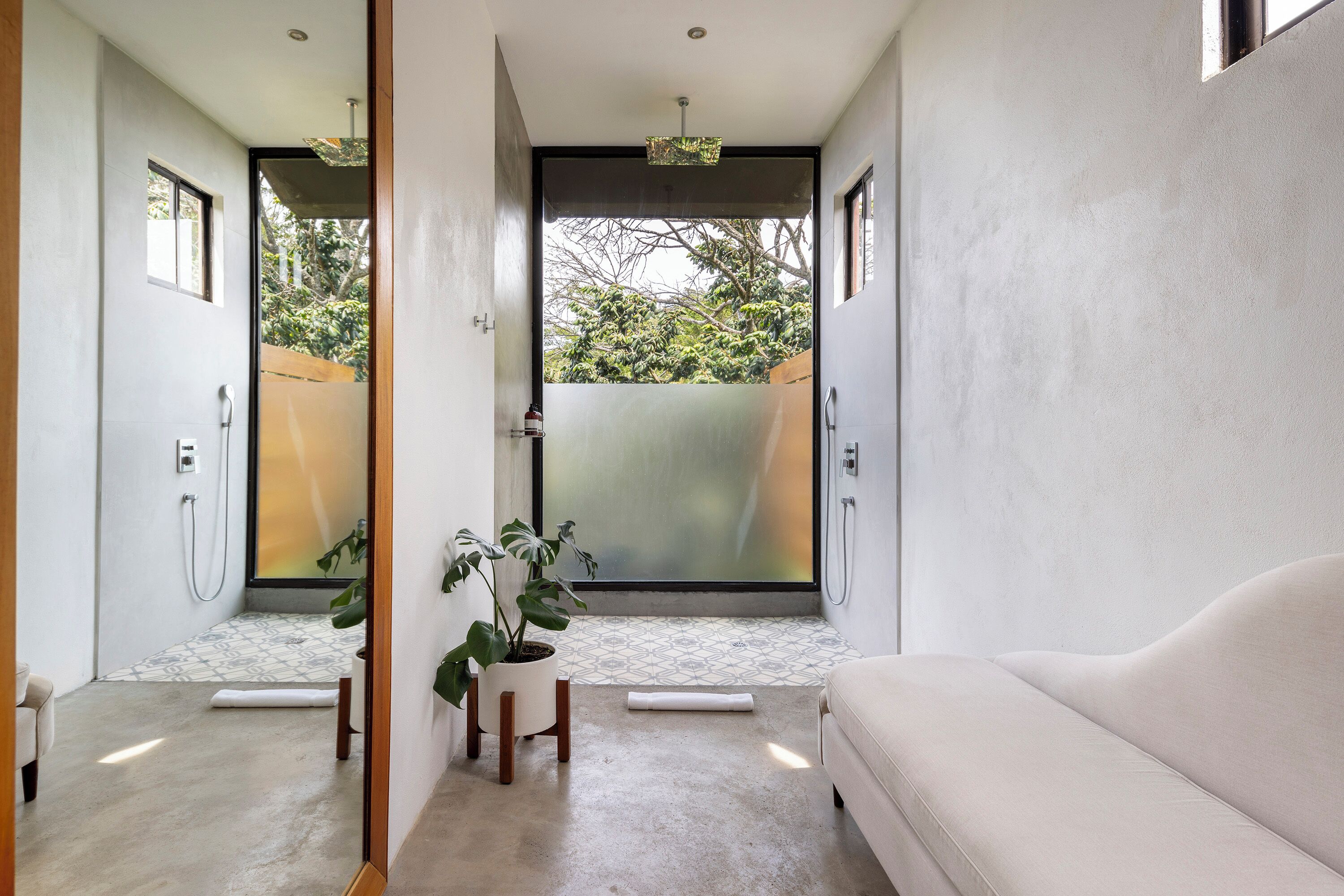 A modern bathroom with a large window, a potted plant, and a white sofa.
