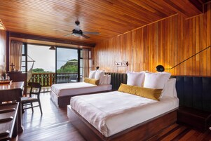 Una habitación con dos camas, suelo de madera, ventilador de techo y vistas amplias por un gran ventanal.