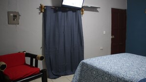 A room with a bed, a red chair, a curtain, and a mounted television. - Private Front Beach House (Huehuete)