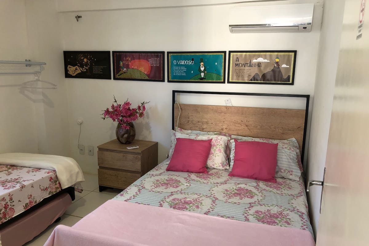 A bedroom with a bed, a nightstand, a vase with flowers, and wall art.