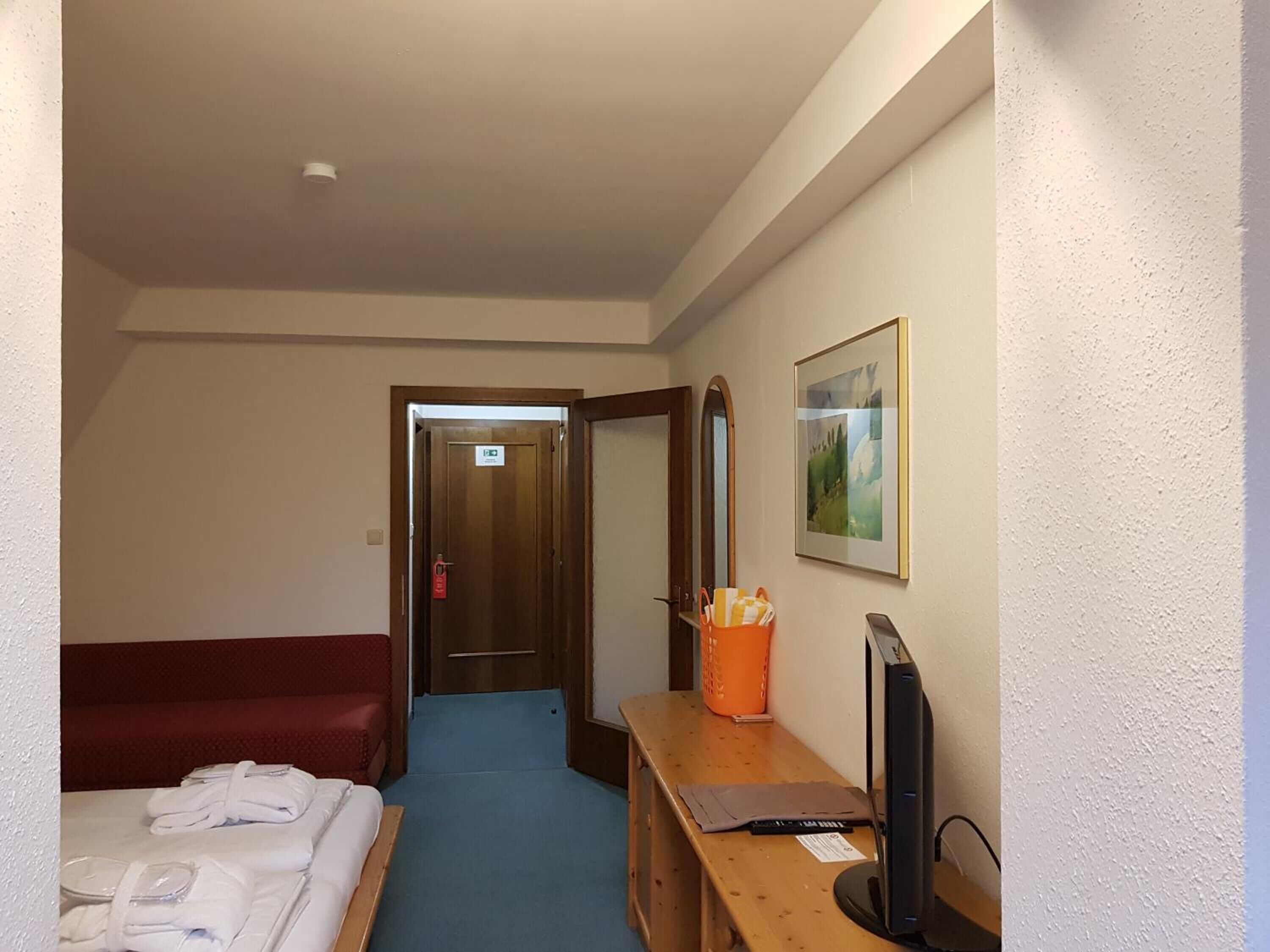 Una habitación de hotel con cama, escritorio con computadora, sofá rojo y pasillo que conduce a otra habitación.