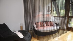 A modern room with a black leather chair, a hanging bed with pink pillows, and a large window. - Hotel Nockalm (Krems in Kaernten)