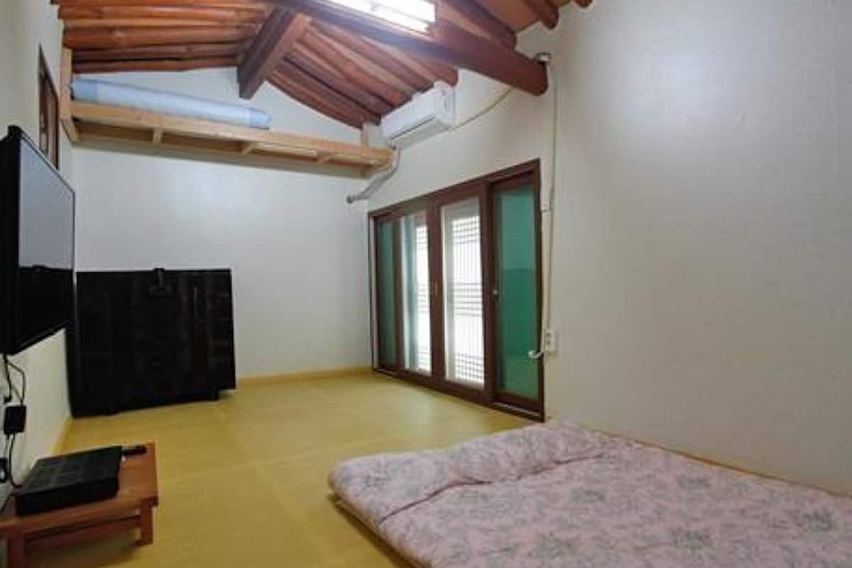 A room with a wooden ceiling, a bed, a desk, and a sliding glass door.