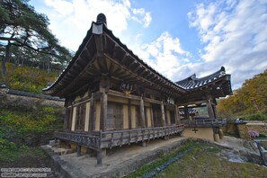 A traditional wooden building with a tiled roof, surrounded by trees and a stone pathway. - Gwiae Traditional House (Yeongcheon)