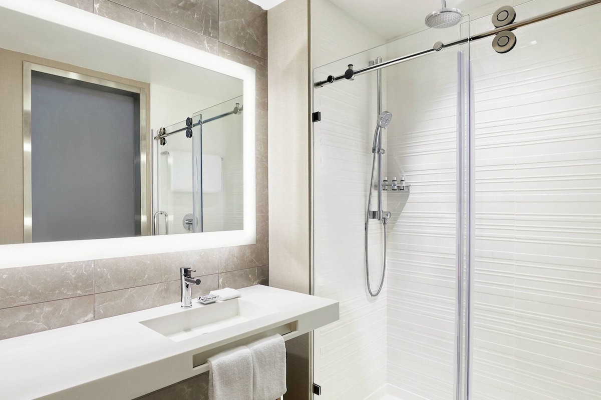 A modern bathroom with a glass shower enclosure, a white sink with a mirror above it, and a towel hanging on the wall.