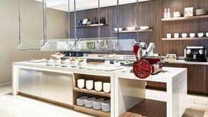 Un comptoir de petit-déjeuner moderne, doté d’une vitrine, d’étagères blanches et en bois, et d’une machine à café rouge.