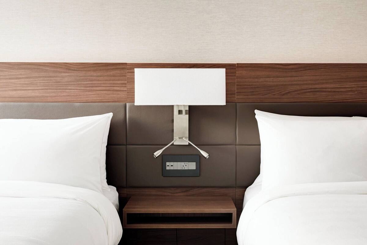 Une chambre d’hôtel avec une tête de lit en bois, une table de chevet et une lampe fixée au mur.