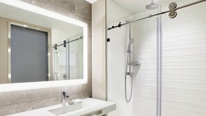Une salle de bain moderne avec un grand miroir, un lavabo et une douche à parois de verre.