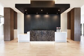 A reception desk with a marble top, flanked by two white counters, in a modern lobby with wooden flooring and dark vertical paneling on the walls. - AC Hotel Huntsville Downtown (Huntsville)