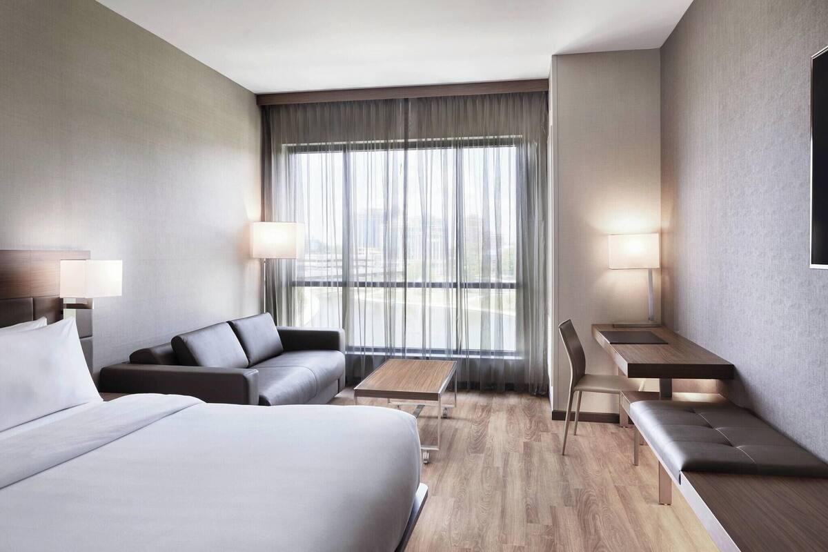 Une chambre d’hôtel moderne avec un grand lit, un canapé, une petite table et un banc.