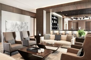 A modern living room with a sofa set, coffee table, and decorative pillows. There is a large abstract painting on the wall and a kitchen area in the background. - AC Hotel Huntsville Downtown (Huntsville)