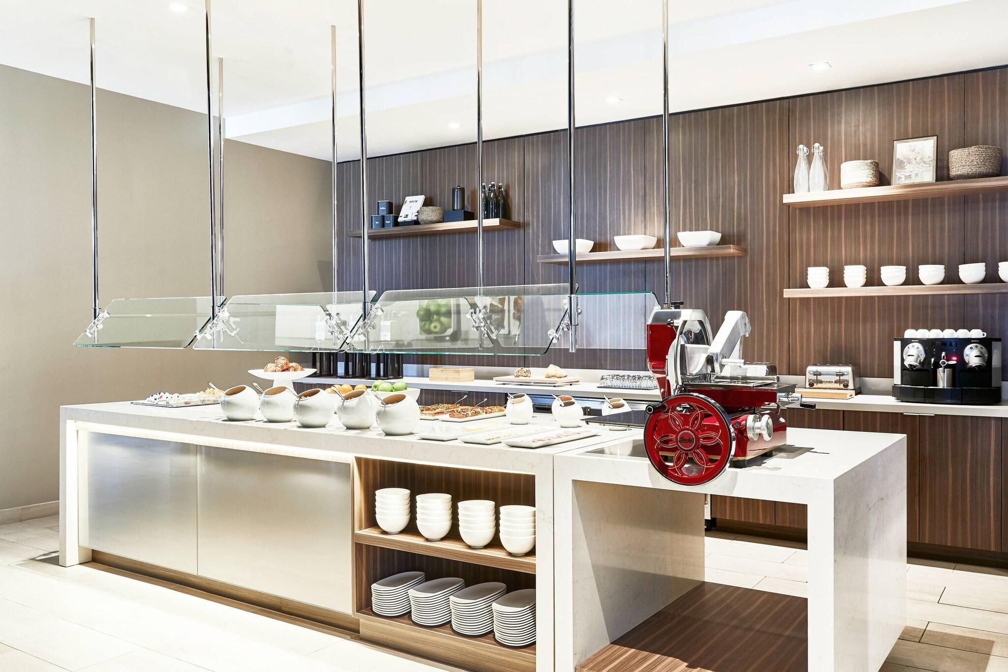 A modern breakfast bar with a coffee machine, a fruit display, and a variety of breakfast items.