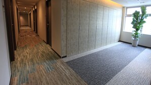 A hotel corridor with carpeted flooring, a potted plant, and a large window. - Urban Hotel Kyoto Gojo Premium (Kyoto)