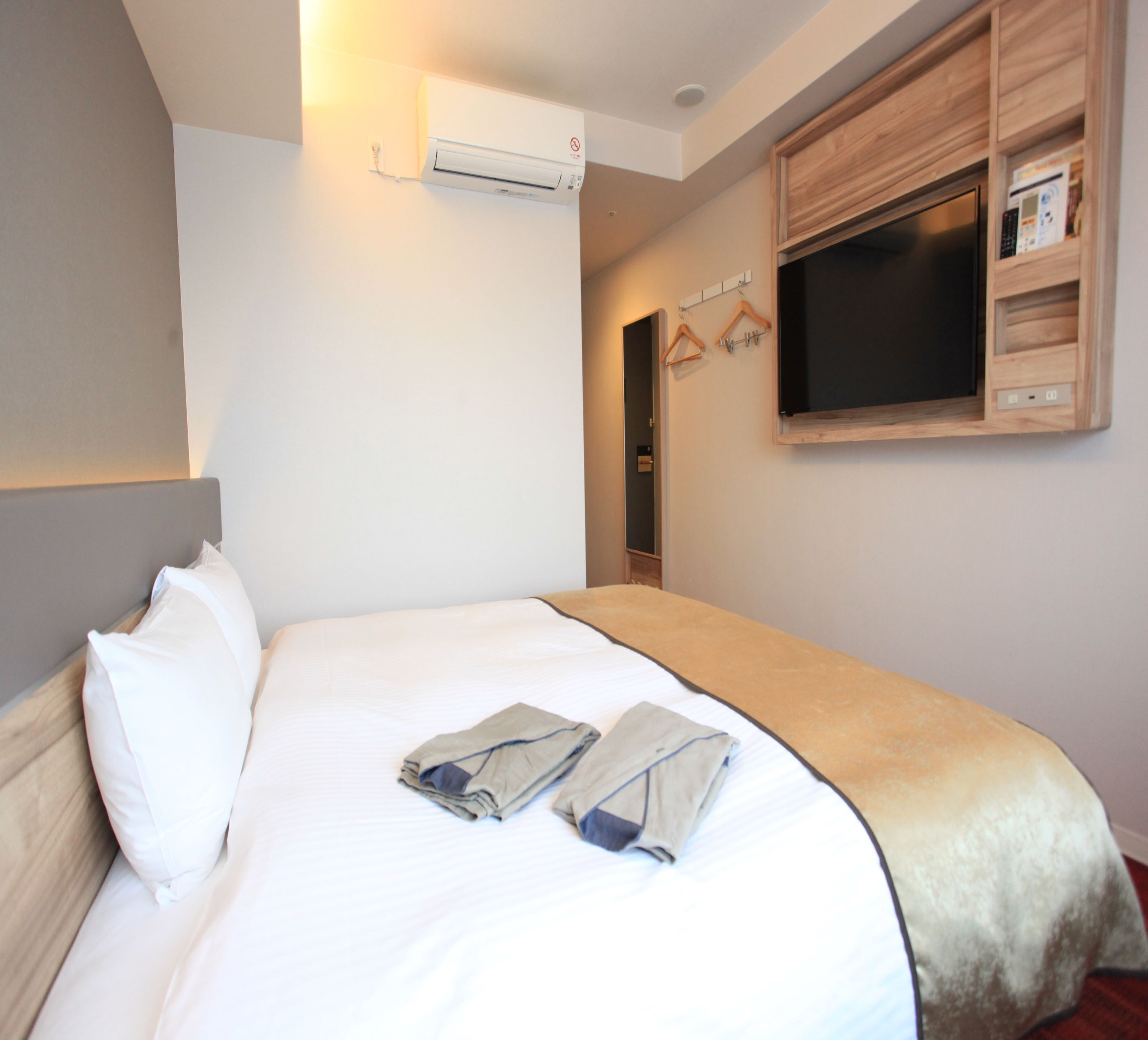 A hotel room with a bed, a TV mounted on the wall, and an air conditioning unit above the bed.