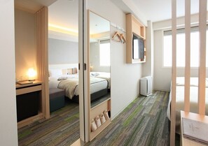 Habitación de hotel con cama, escritorio, espejo, televisor y zapatero.