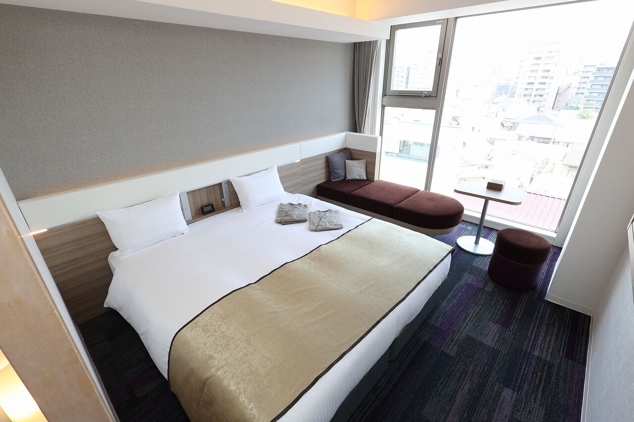 Ein Hotelzimmer mit einem großen Bett, einem kleinen Sofa, einem Beistelltisch und einem Fenster mit Blick auf die Stadt.