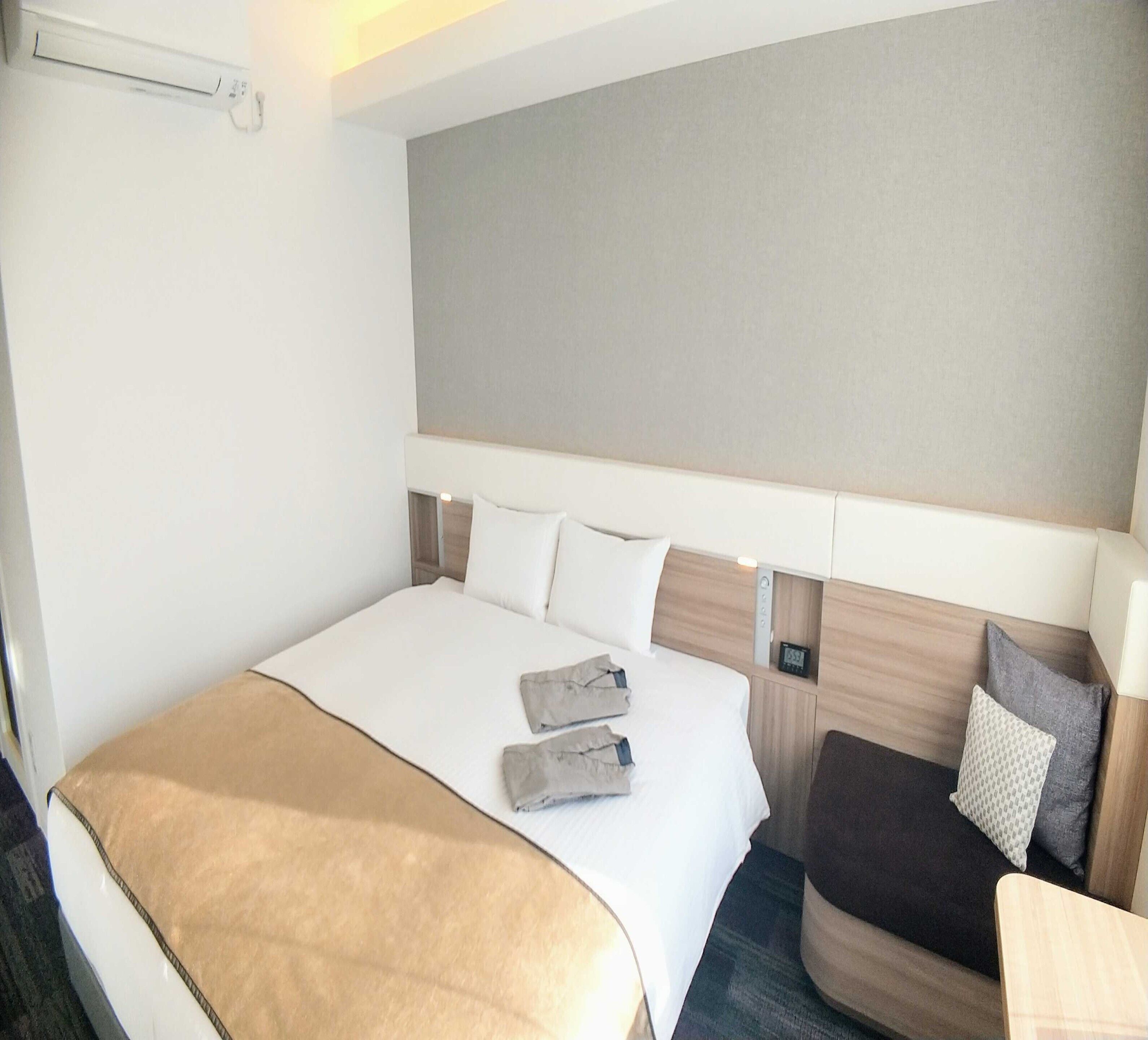 A hotel room with a large bed, a bedside table, a chair, and a headboard.