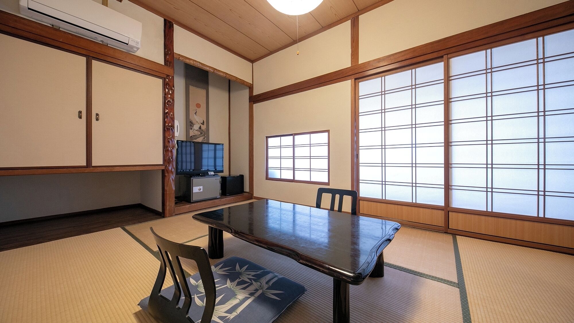 A traditional Japanese room with tatami flooring, a low table, chairs, a television, and sliding doors.