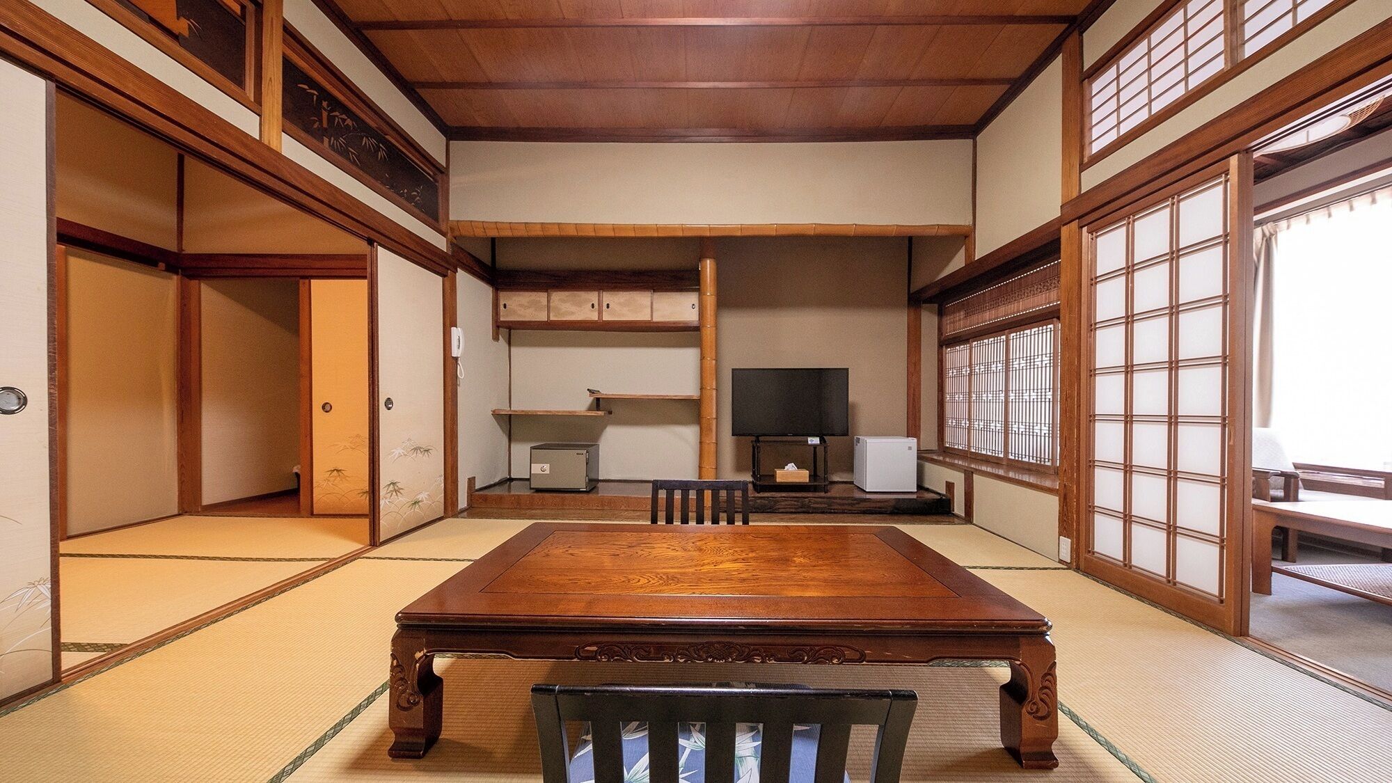 A traditional Japanese room with tatami flooring, a wooden table, a television, and sliding doors.